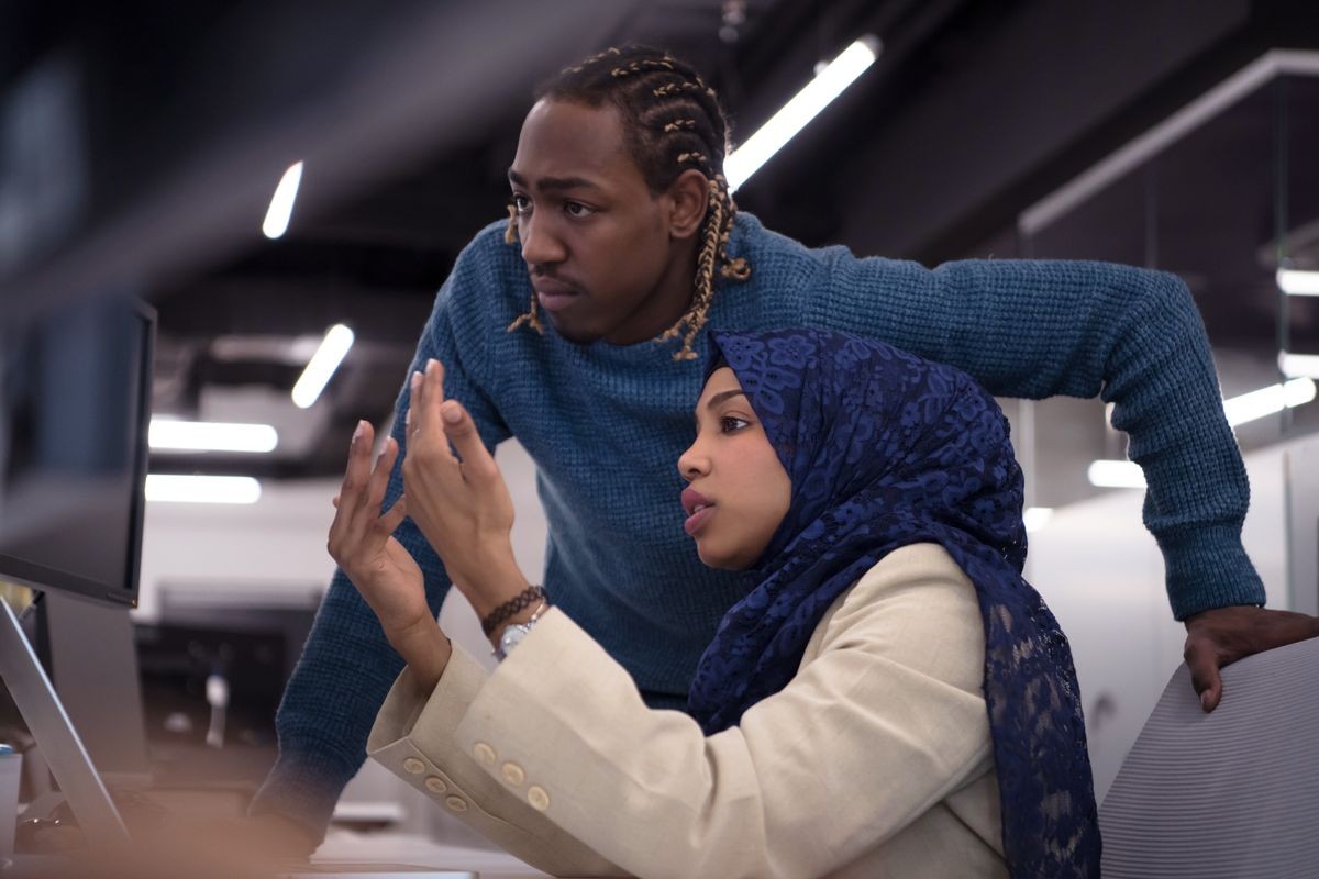 black muslim female software developer working together with her african american male colleague using computer while writing programming code at modern startup office